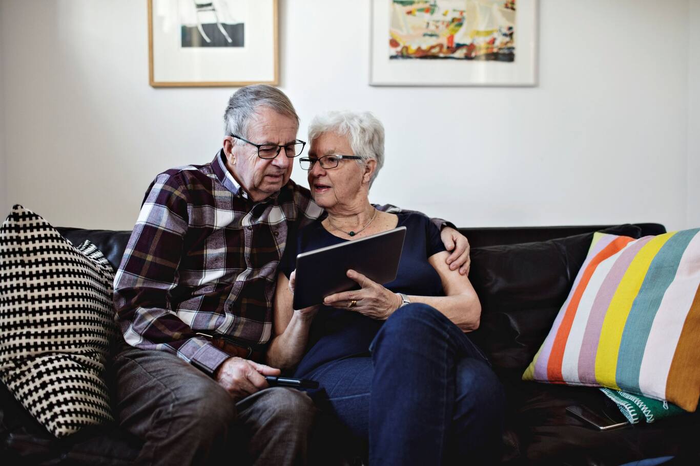 dvaja seniori sedia na pohovke a pozerajú na tablet