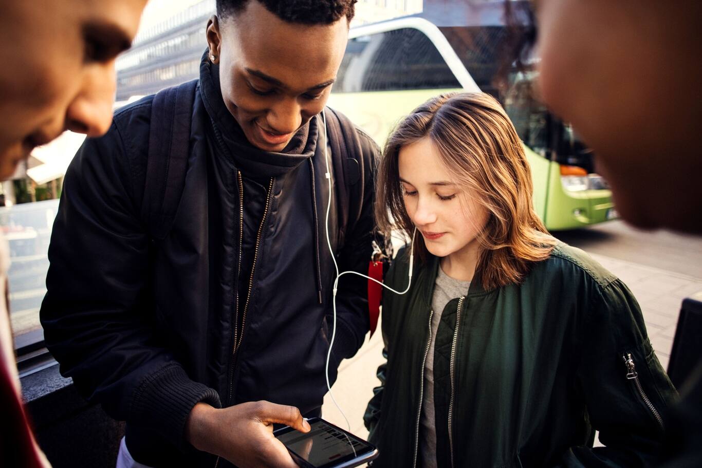 Skupina mladých kamarátov na ulici s mobilom v ruke a slúchadlách v ušiach