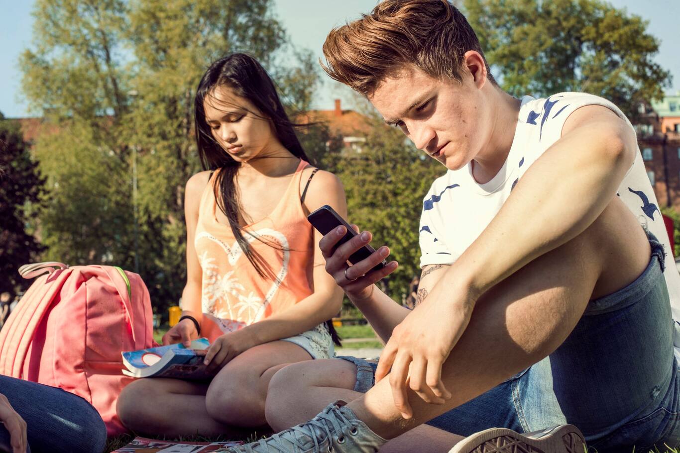Dievča a chlapec z generácie Z v parku a s mobilom v ruke
