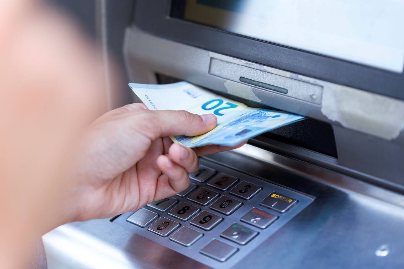 Ruka vyťahujúca 20-eurové bankovky z bankomatu.