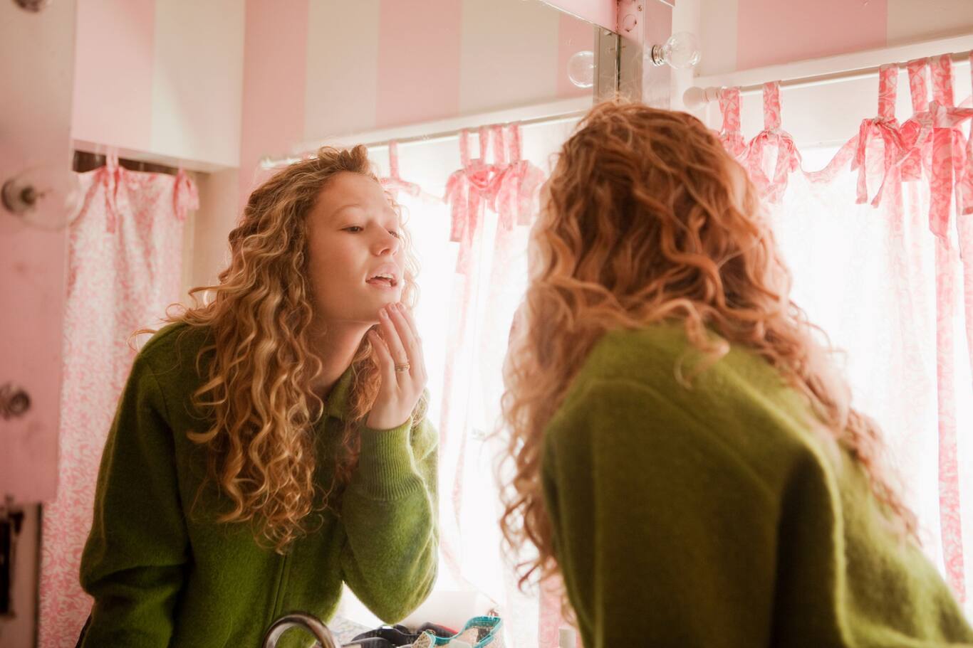 Mladé dievča, ktoré si robí jej skincare rutinu v zrkadle