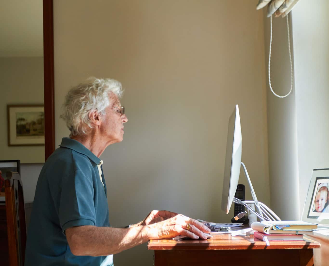 Seniorka, ktorá sedí za počítačom v obývačke